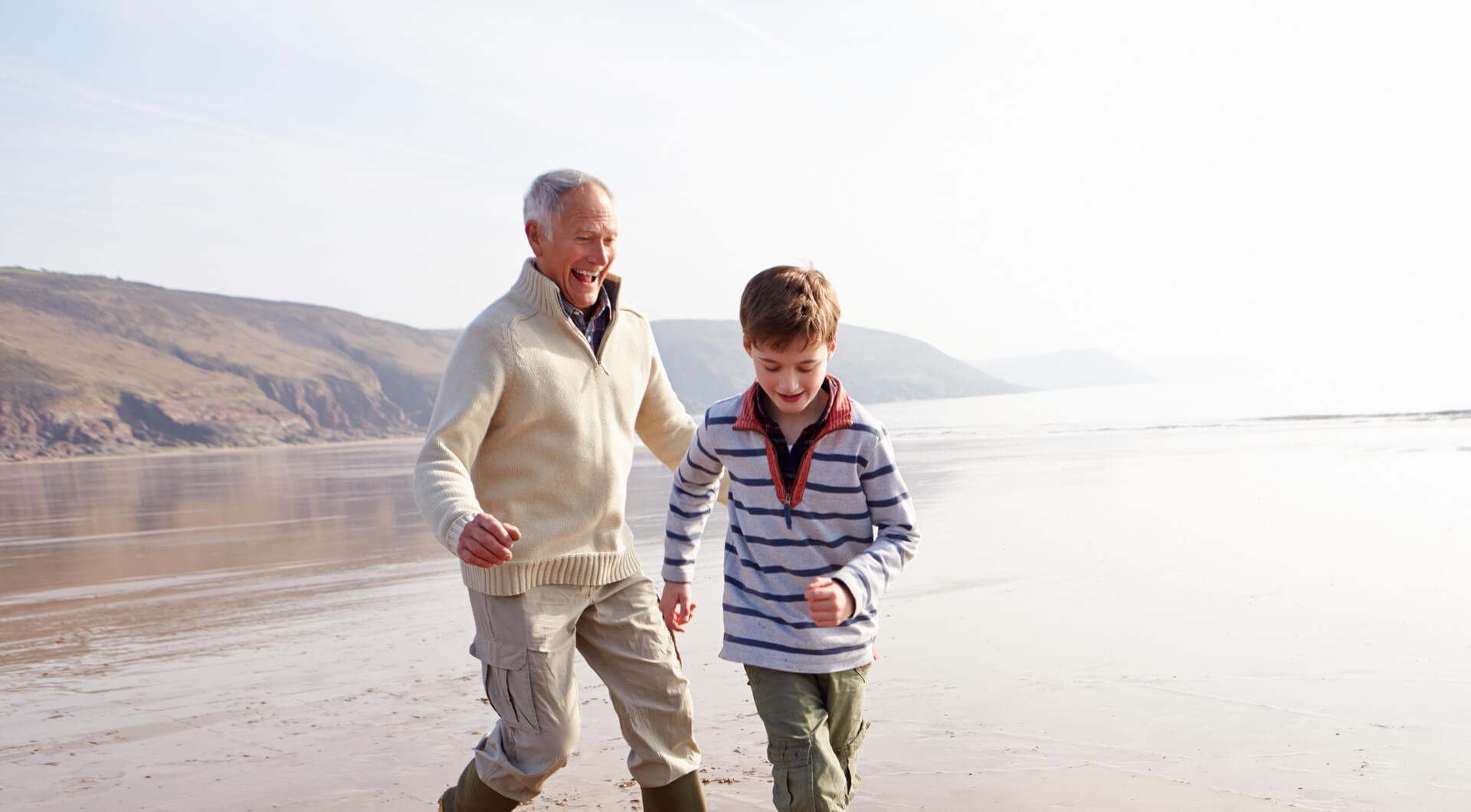 A grandfather and his grandson playing football on a beach.